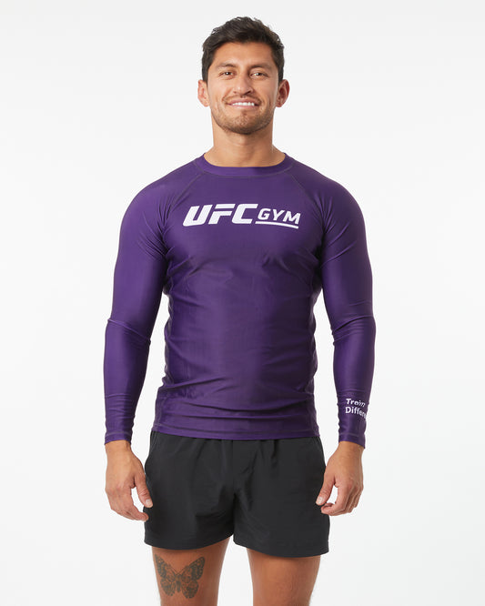 Man wearing a purple UFC Gym long-sleeve shirt and black shorts on a white background facing forward arms down