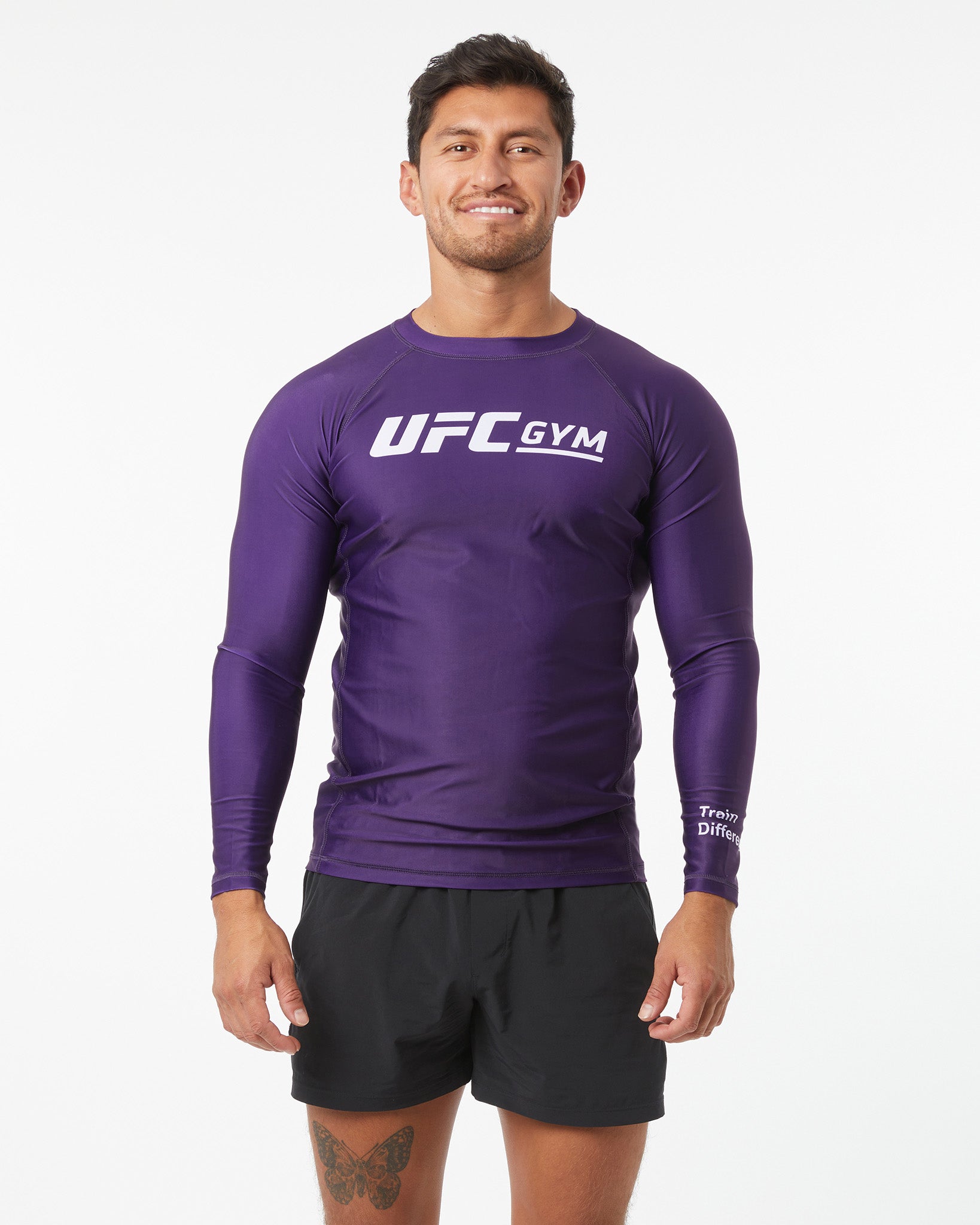 Man wearing a purple UFC Gym long-sleeve shirt and black shorts on a white background facing forward arms down