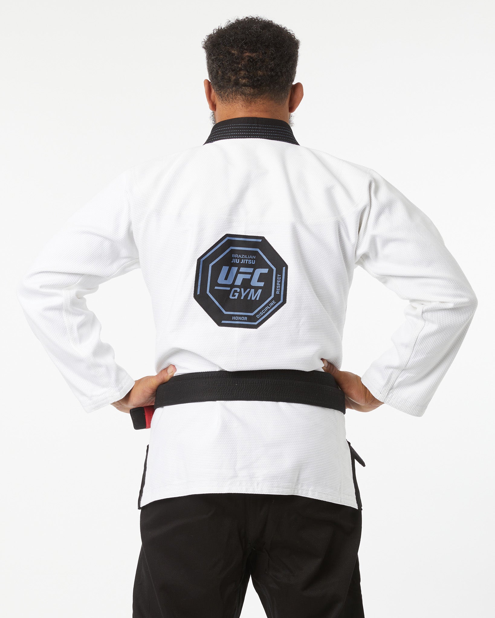 Person wearing a white UFC Gym jacket with a black belt on a white background back logo showing