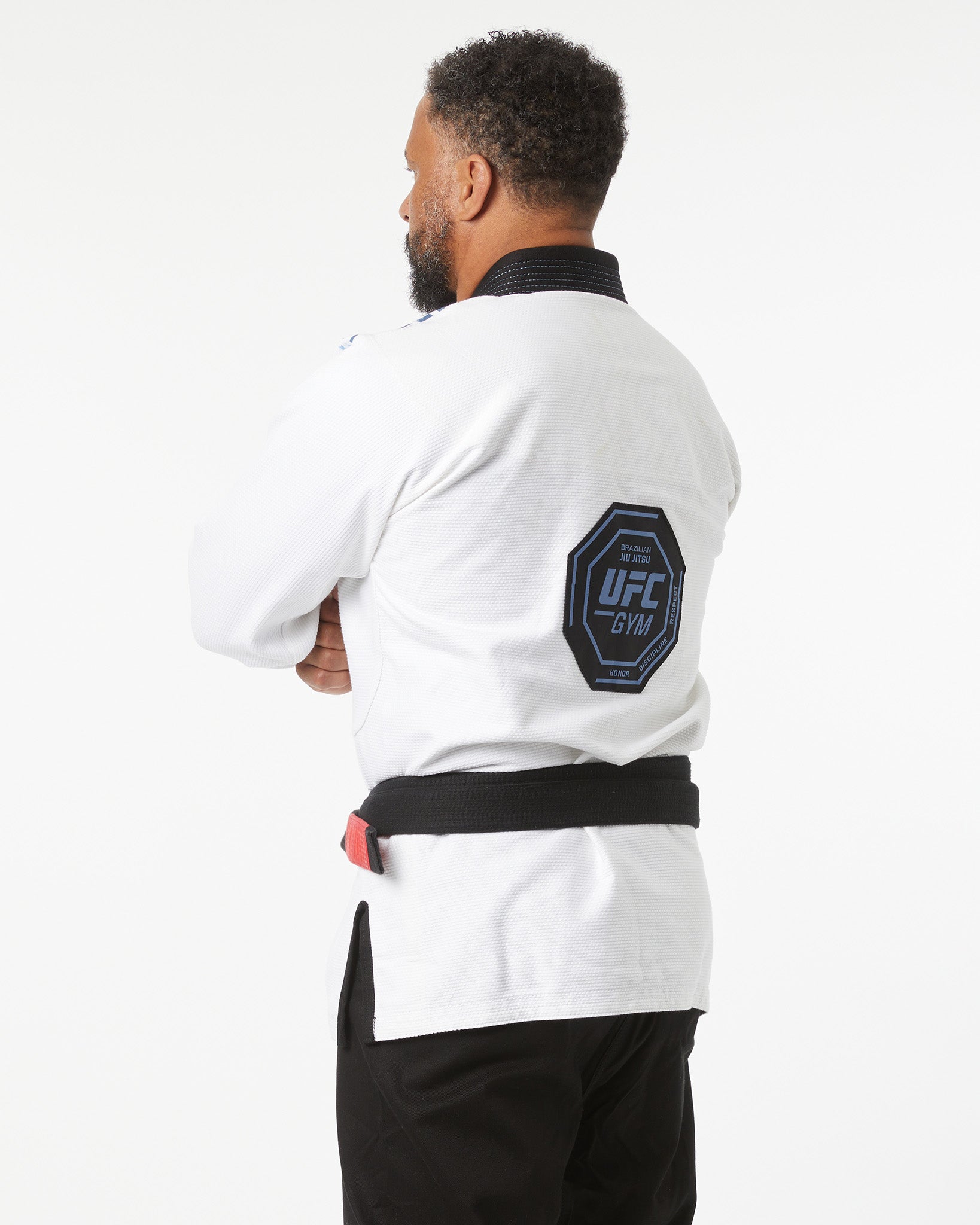 Person wearing a white UFC Gym jacket with a logo on the sleeve against a white background side slightly facing backwards