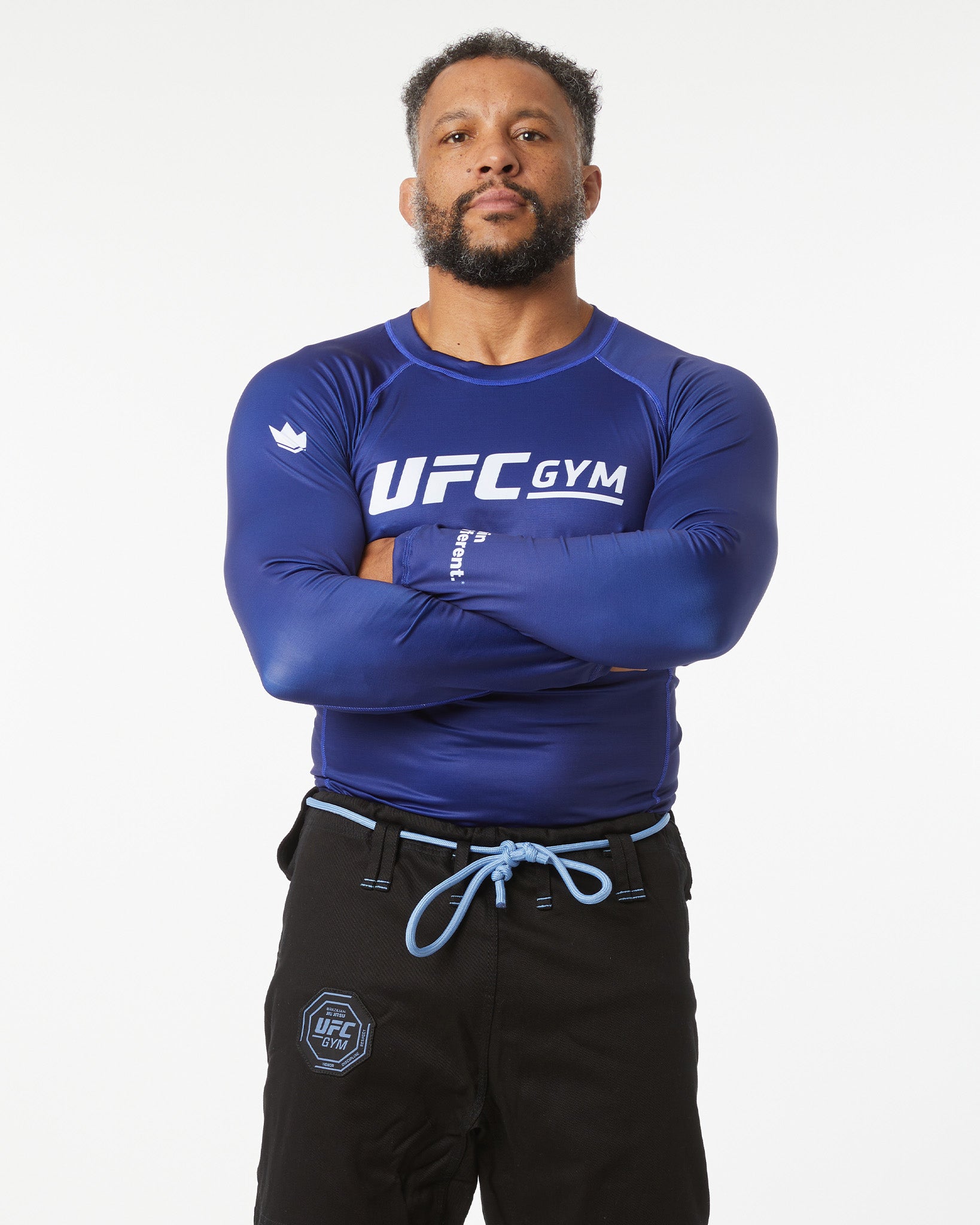 Person wearing a blue UFC Gym shirt with arms crossed on a white background