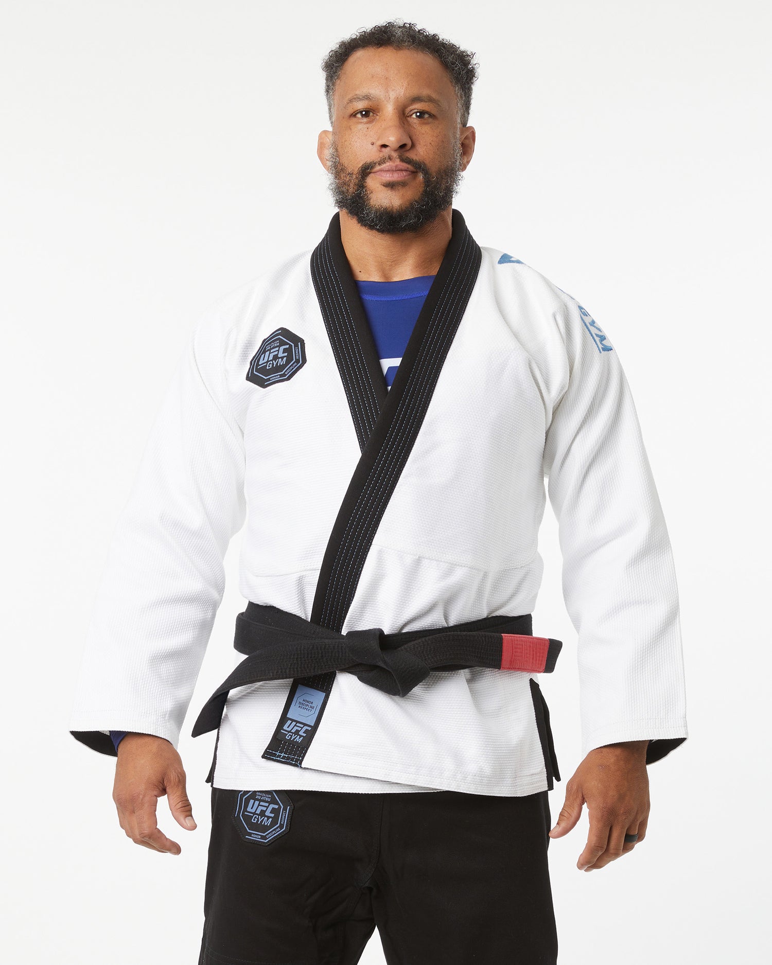 Man wearing a white martial arts uniform with a black belt on a white background zoomed in slightly