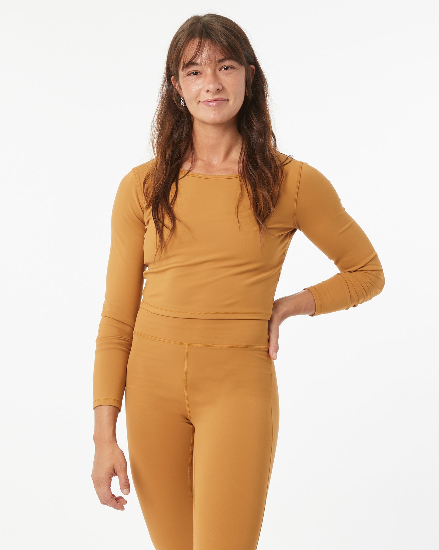 Woman wearing a bronze long sleeve shirt and bronze leggings on a white background