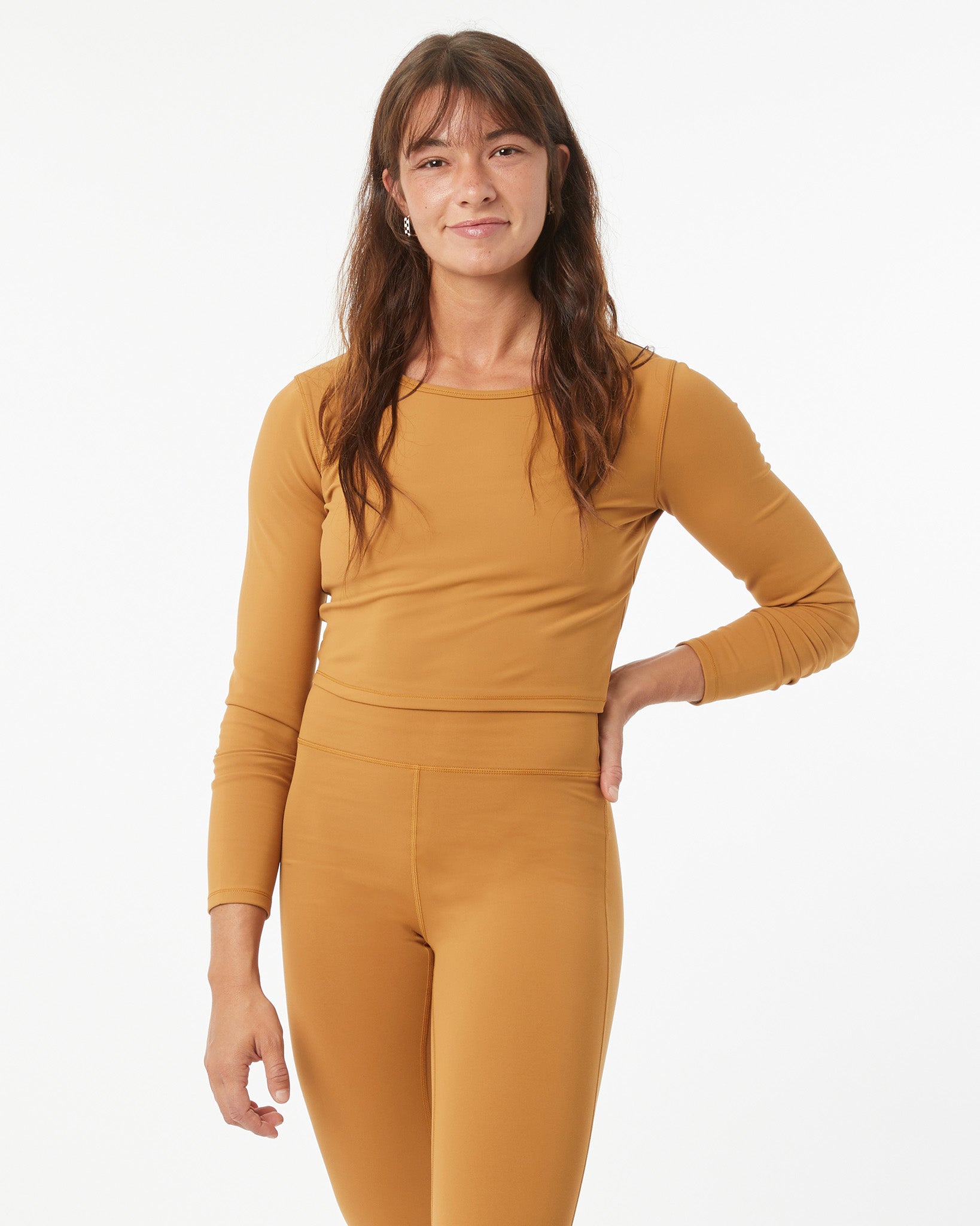 Woman wearing a bronze long sleeve shirt and bronze leggings on a white background