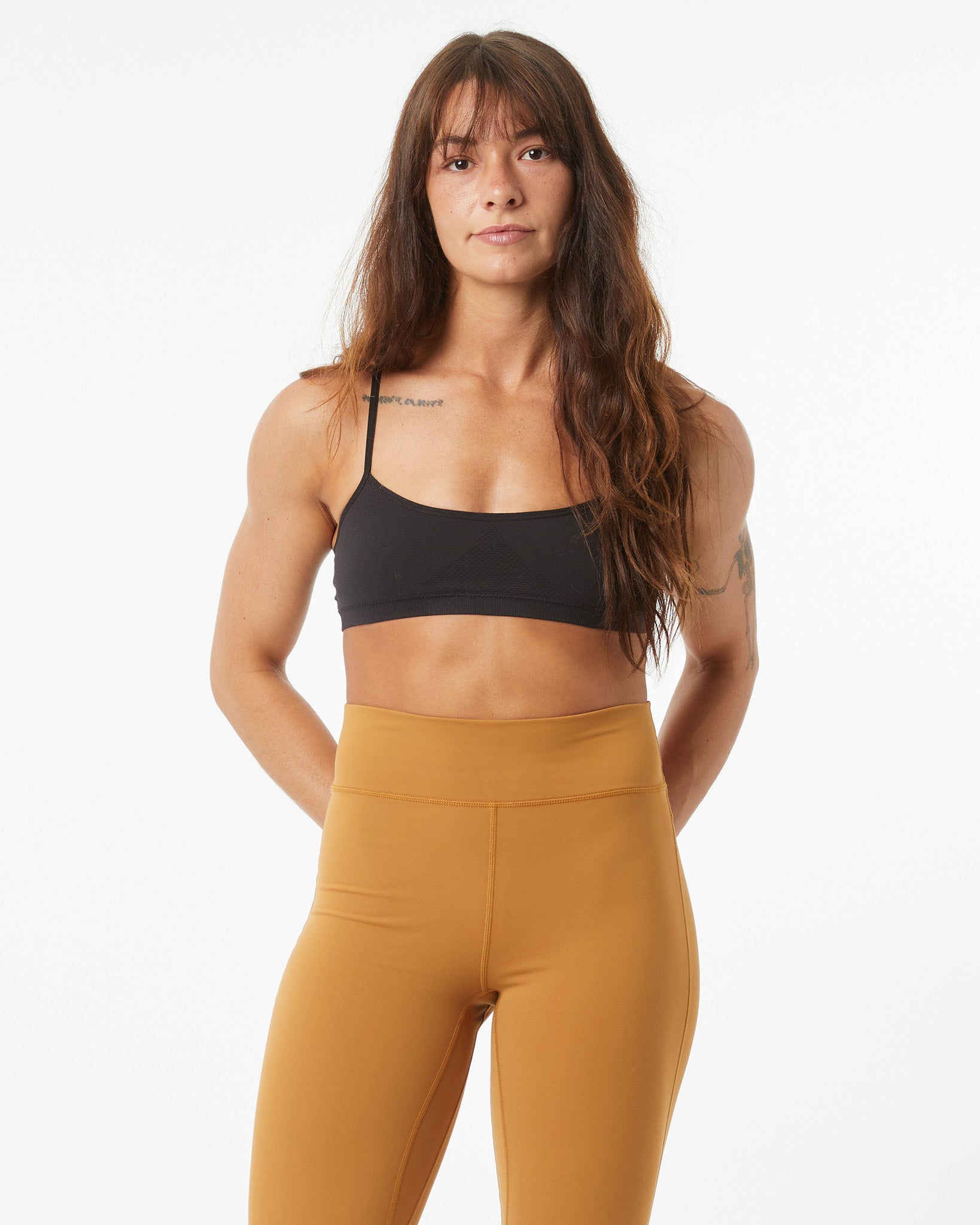 Woman wearing a black sports bra and bronze leggings on a white background