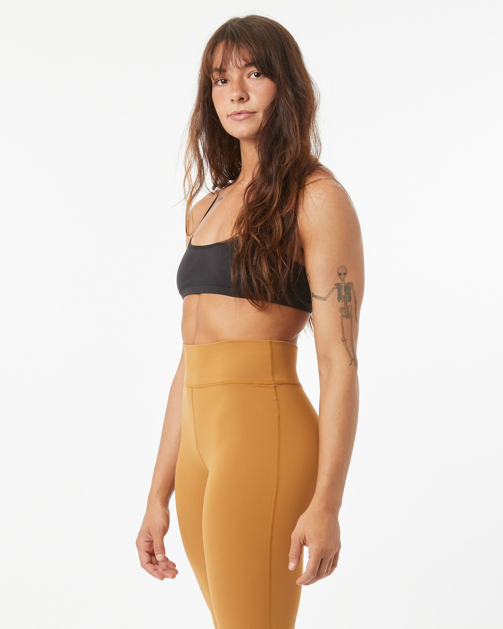 Woman wearing a black sports bra and bronze leggings on a white background