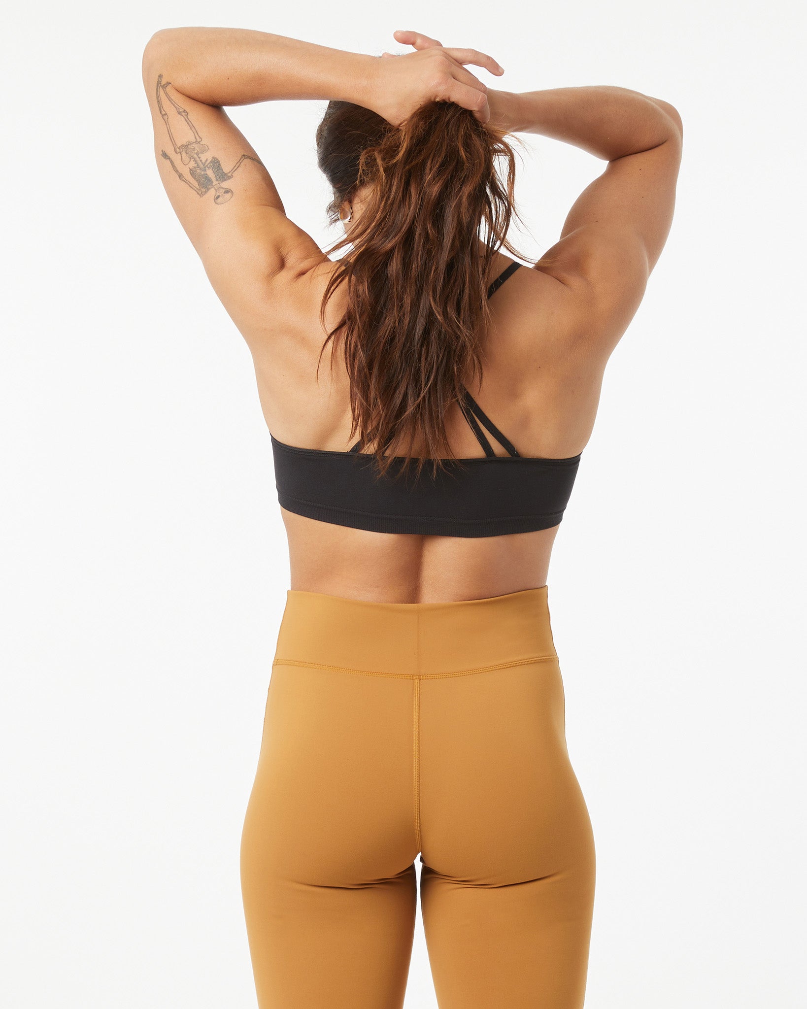 Woman wearing a black sports bra and bronze leggings on a white background