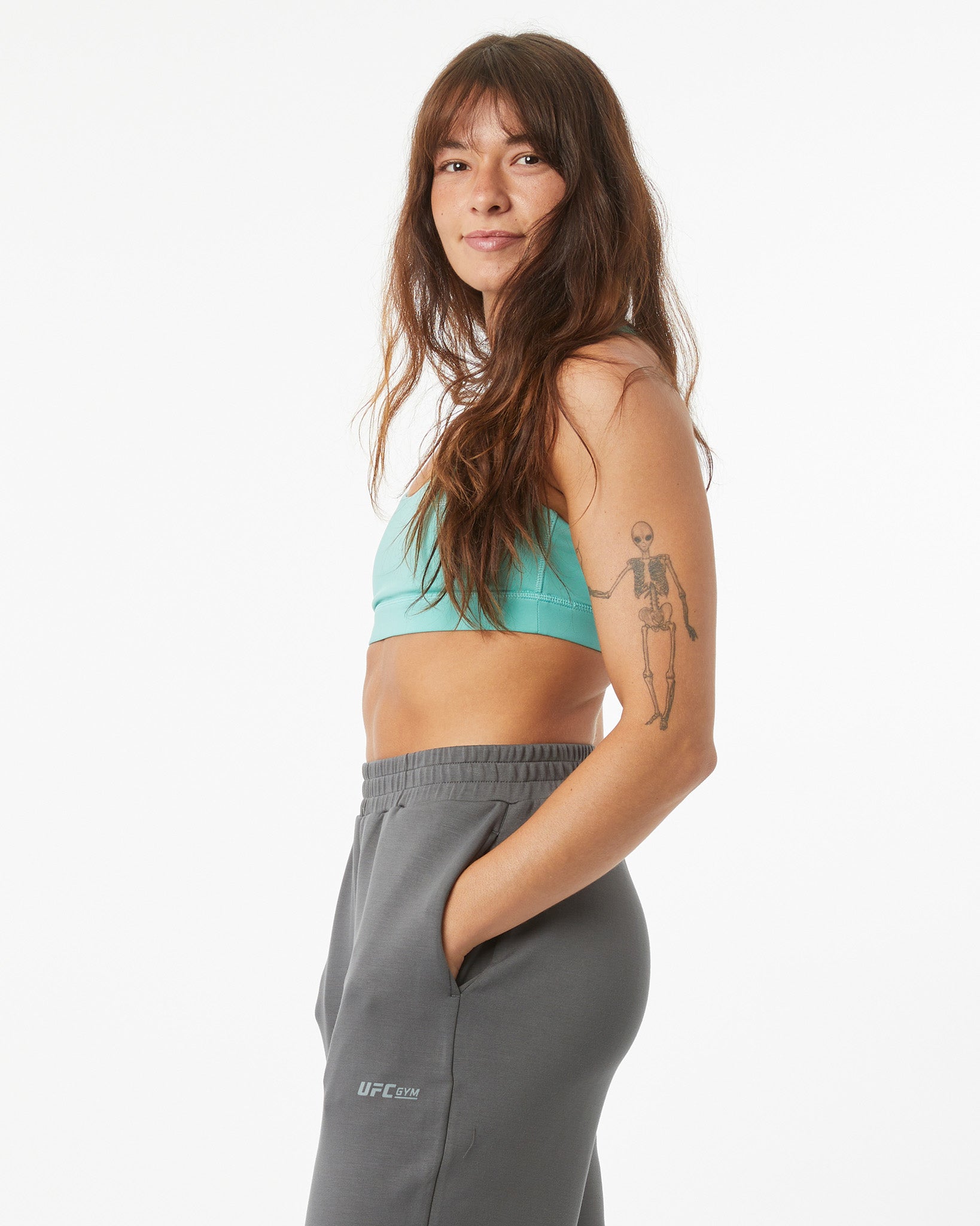 Woman wearing a teal sports bra and gray sweatpants on a white background