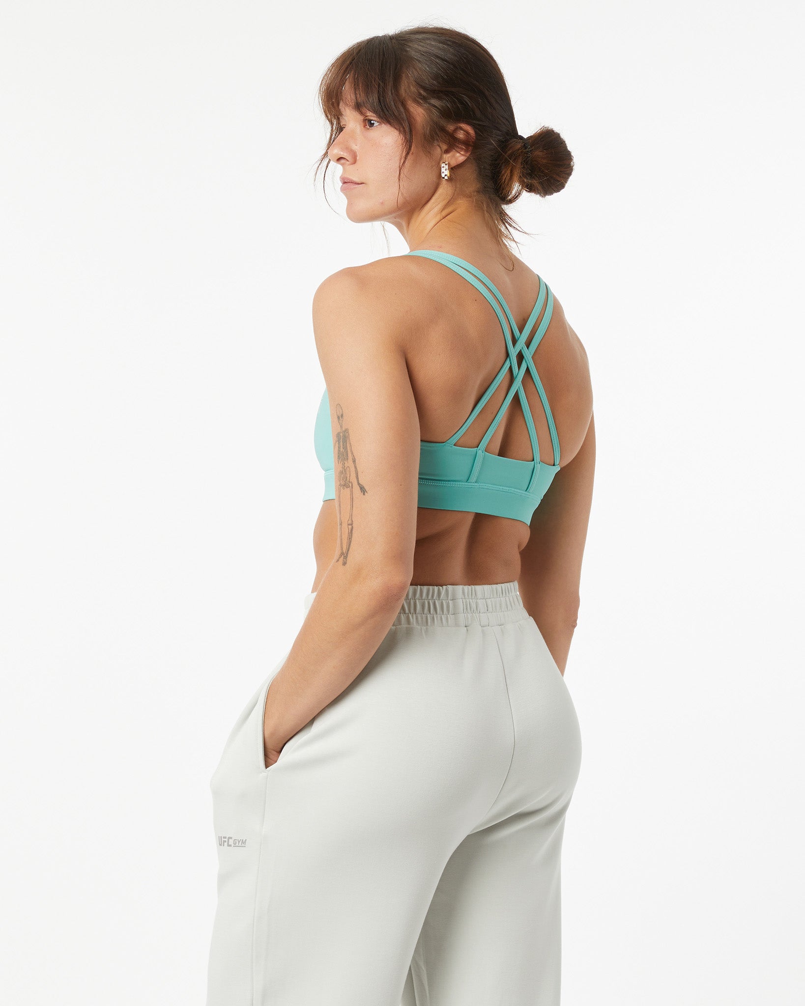 Woman wearing a turquoise sports bra and white pants on a white background