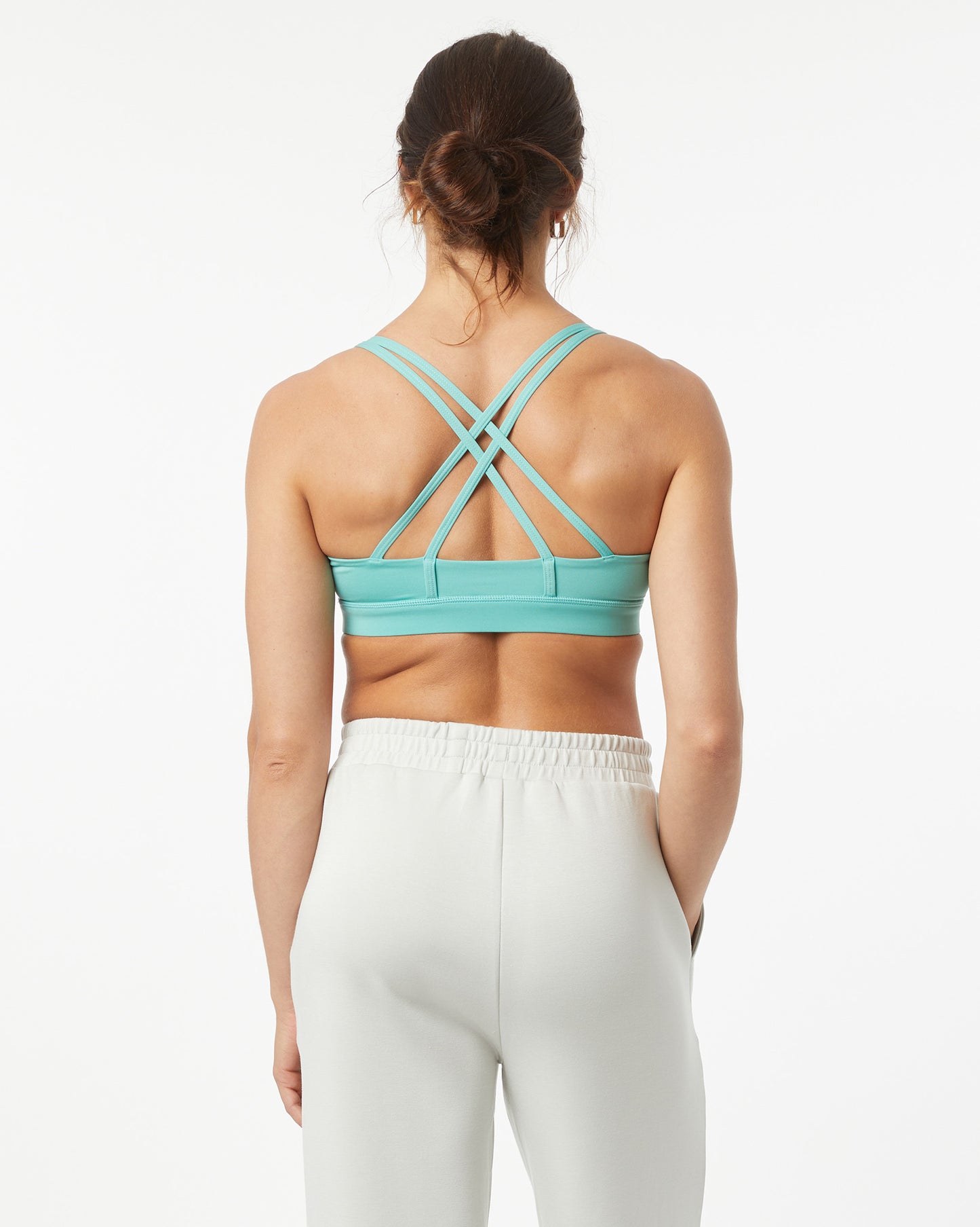 Woman wearing a turquoise sports bra and white leggings on a white background