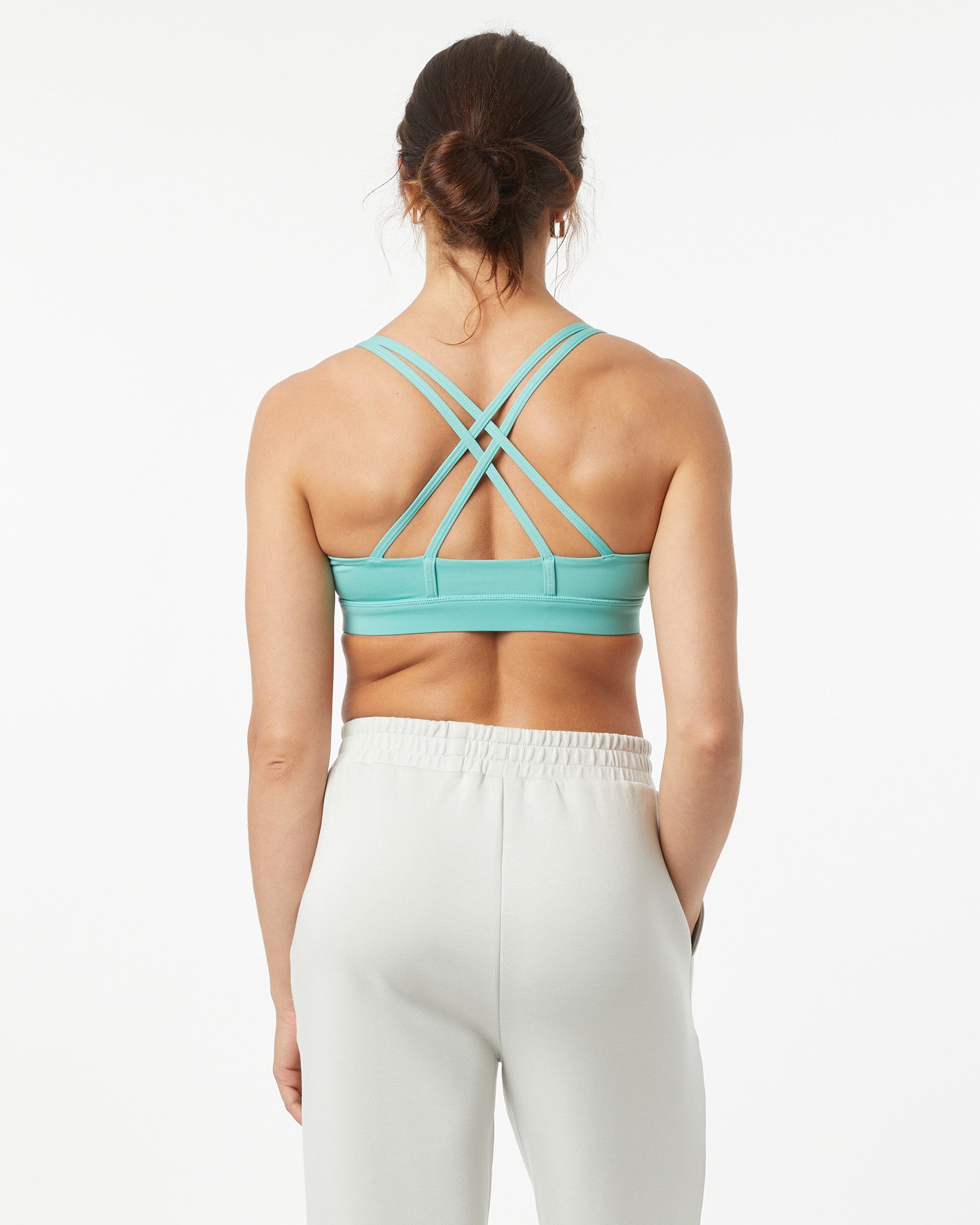 Woman wearing a turquoise sports bra and white leggings on a white background