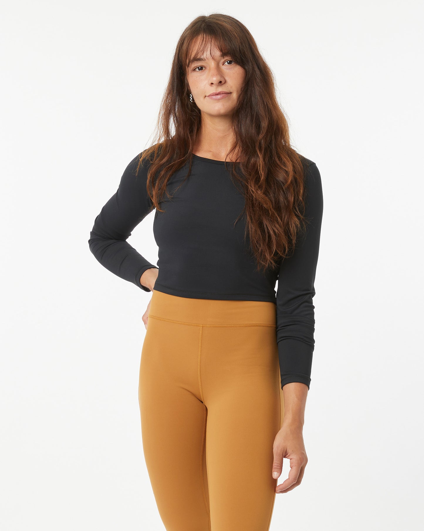 Woman wearing a black long-sleeve crop-top and bronze leggings on a white background