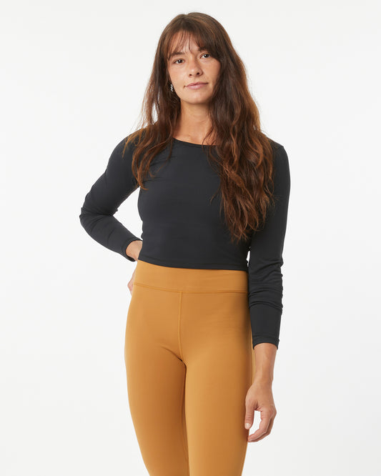 Woman wearing a black long-sleeve crop-top and bronze leggings on a white background