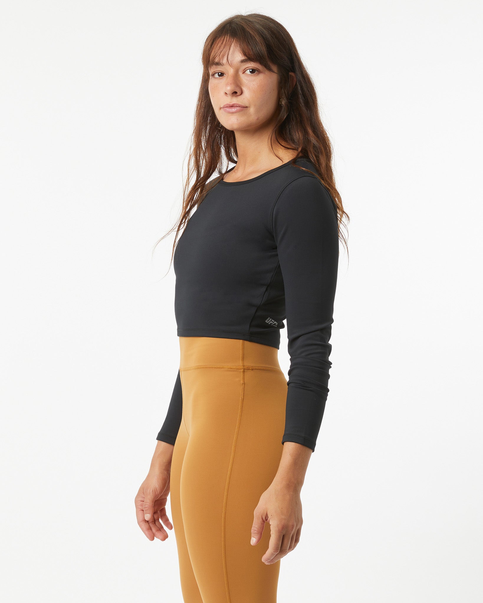 Woman wearing a black long-sleeve crop-top and bronze leggings on a white background