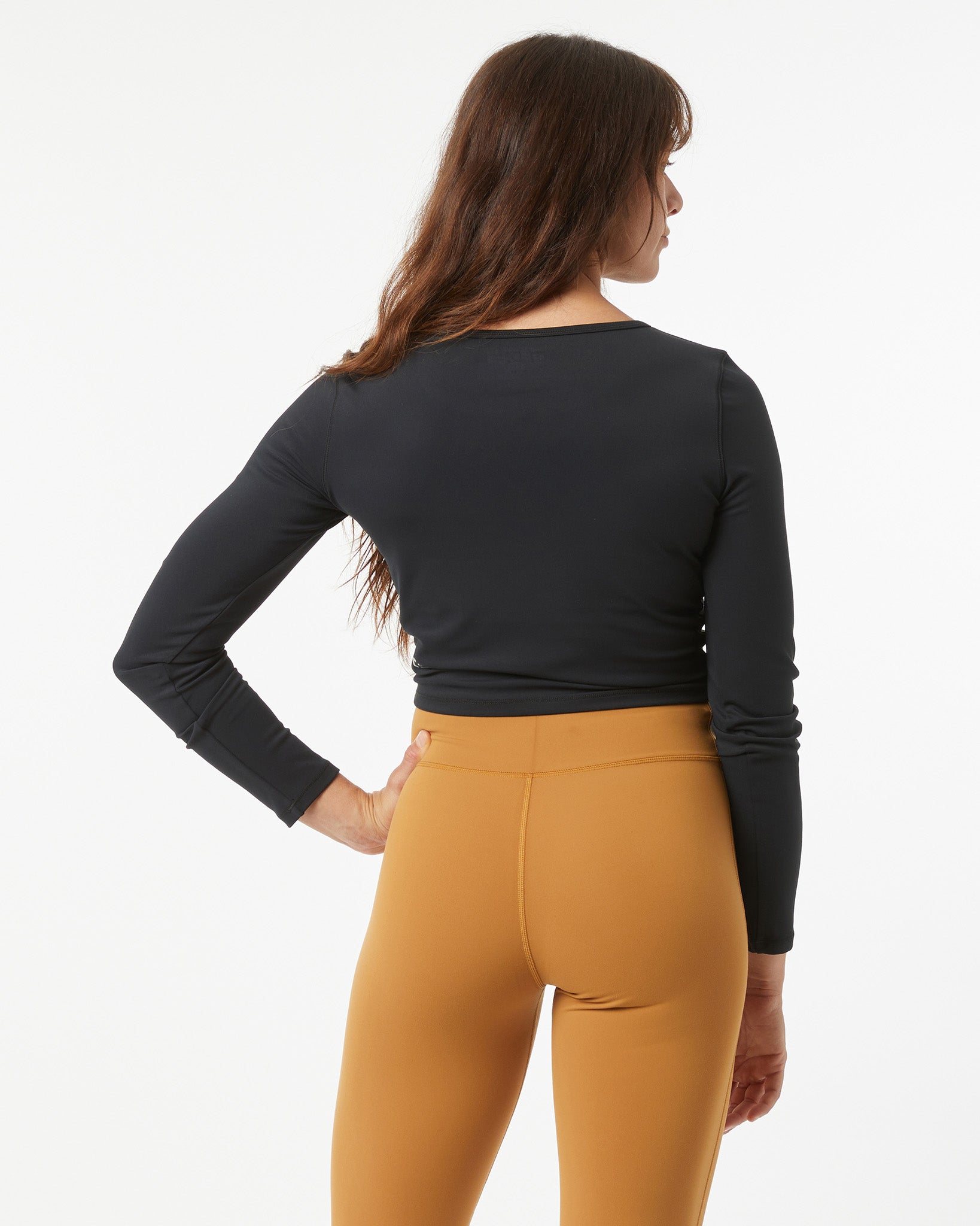 Woman wearing a black long-sleeve crop-top and bronze leggings on a white background