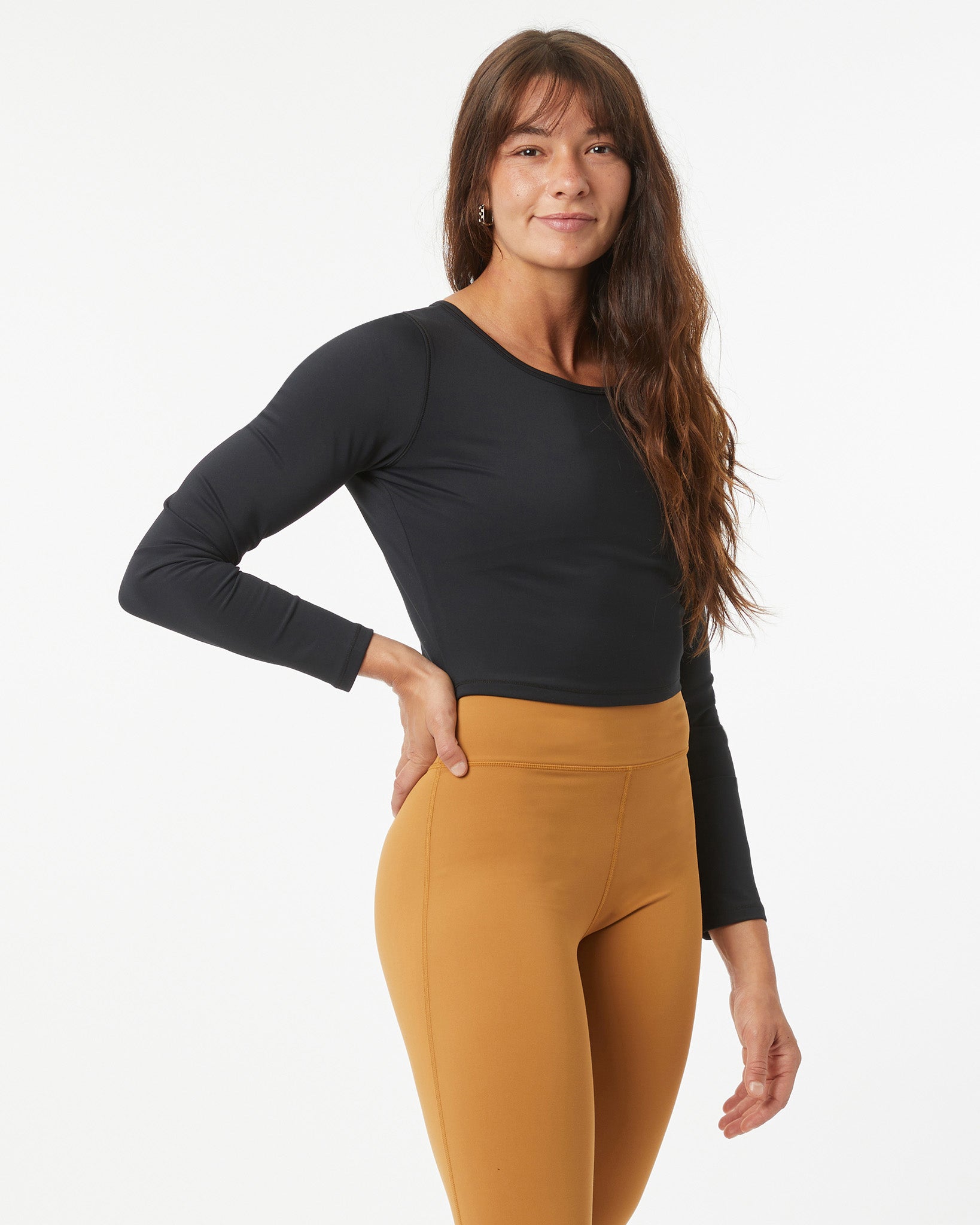 Woman wearing a black long-sleeve crop-top and bronze leggings on a white background