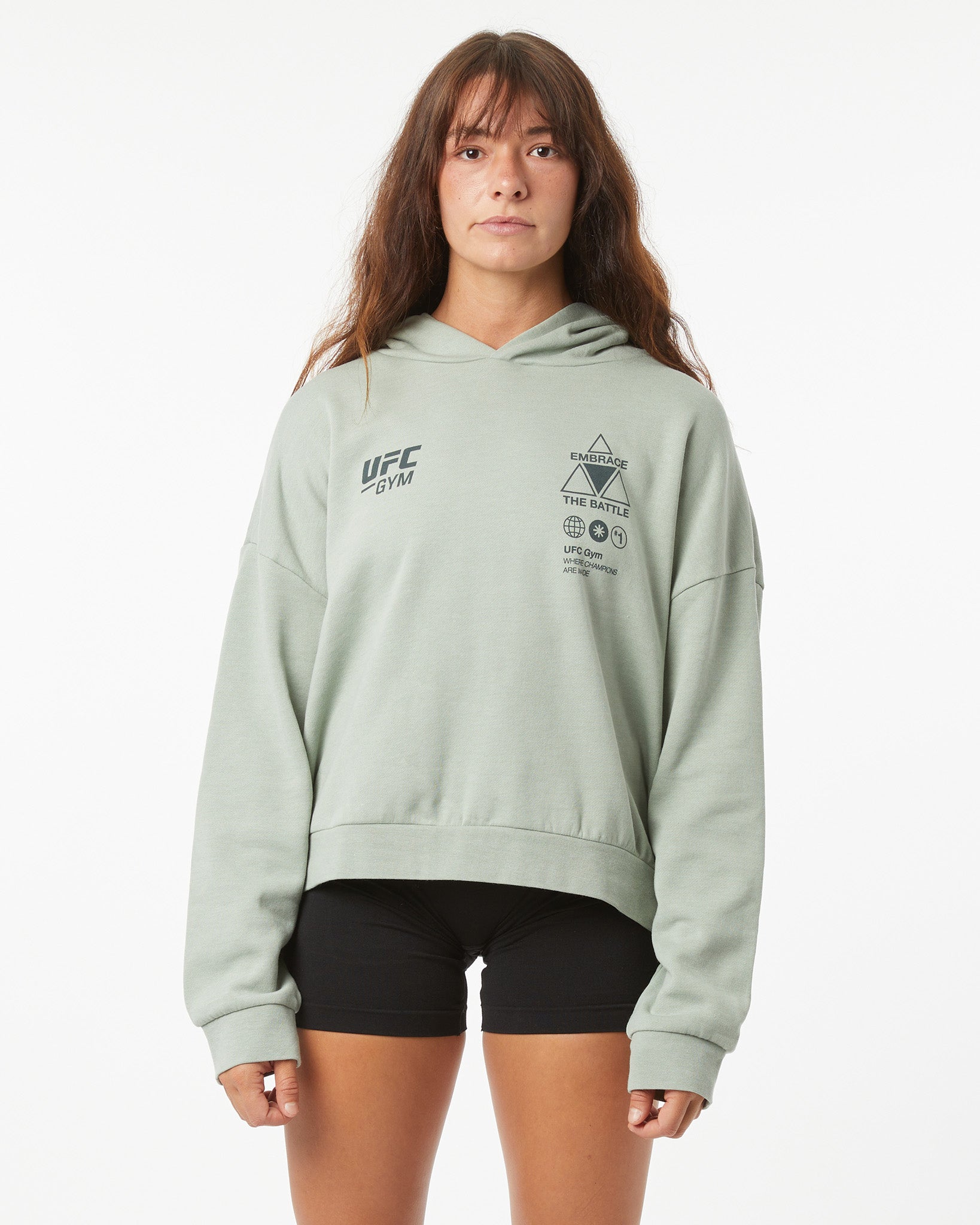 Woman wearing a light green UFC hoodie on a white background facing forward with arms by her sides