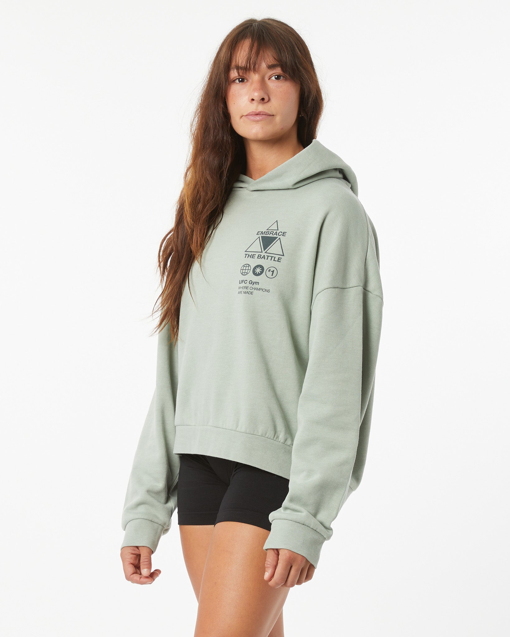 Woman wearing a light green UFC hoodie on a white background facing left, looking forward