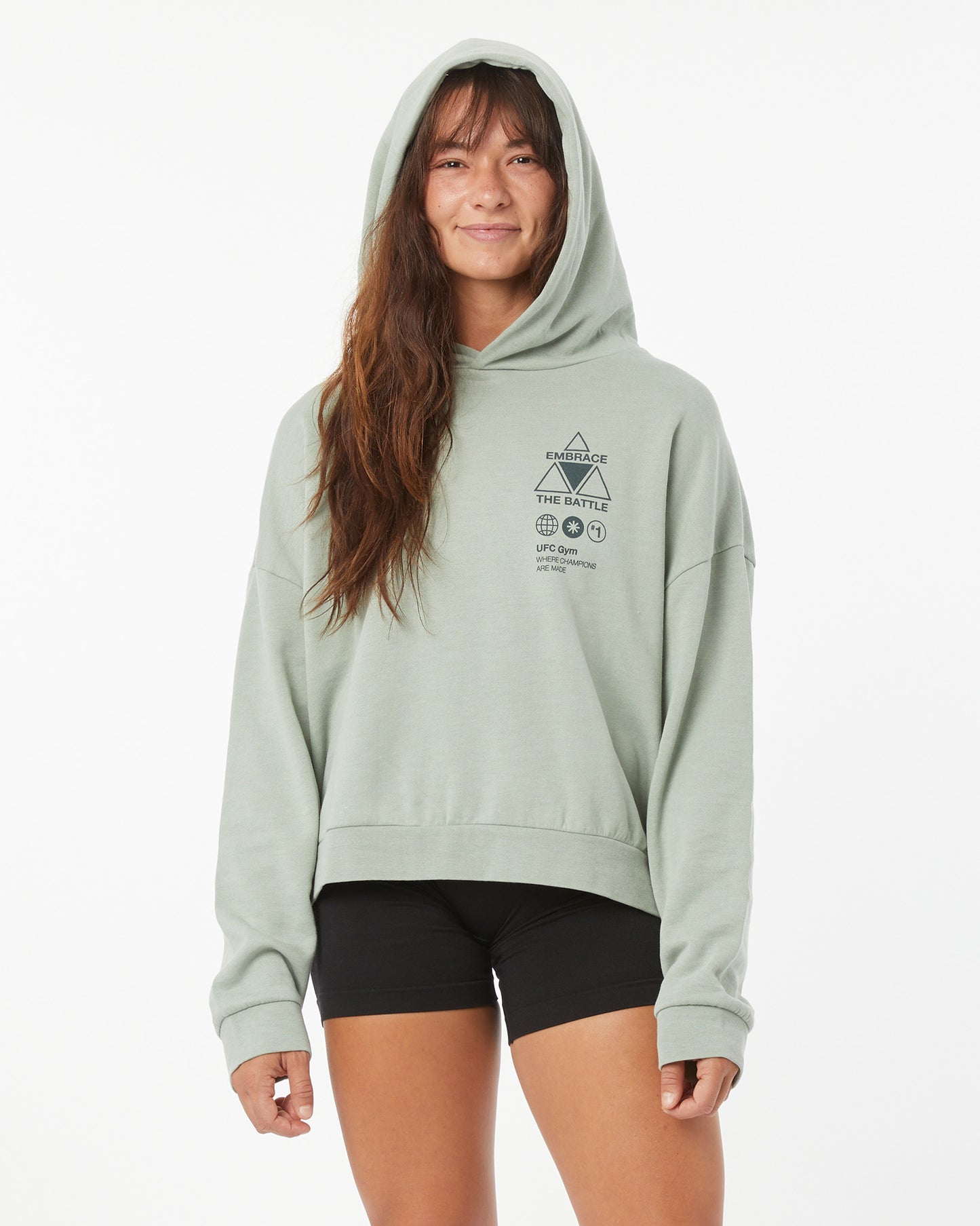 Woman wearing a light green UFC hoodie on a white background with her hood up