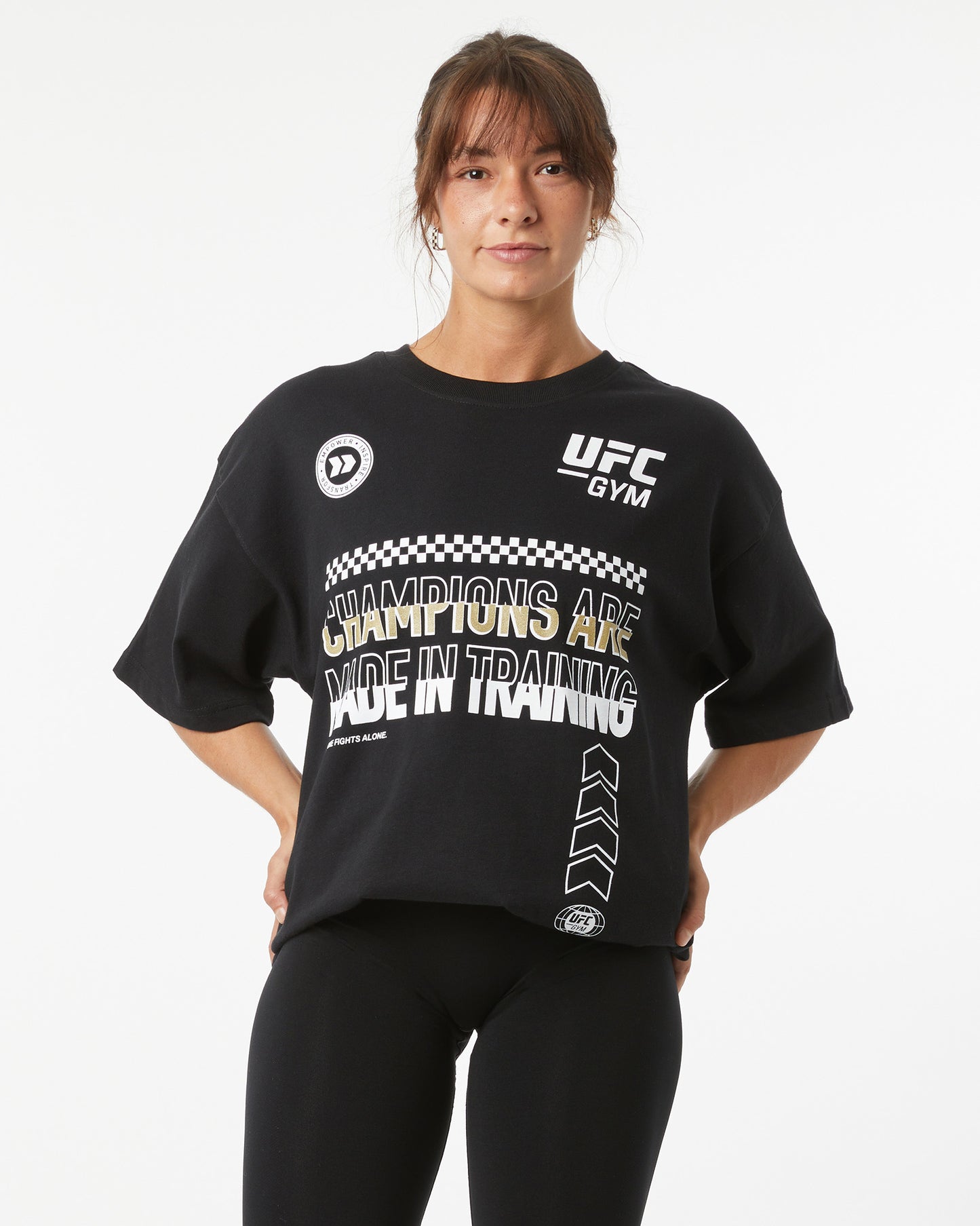 Person wearing a black UFC Gym t-shirt with text on a white background with her hands on her hips