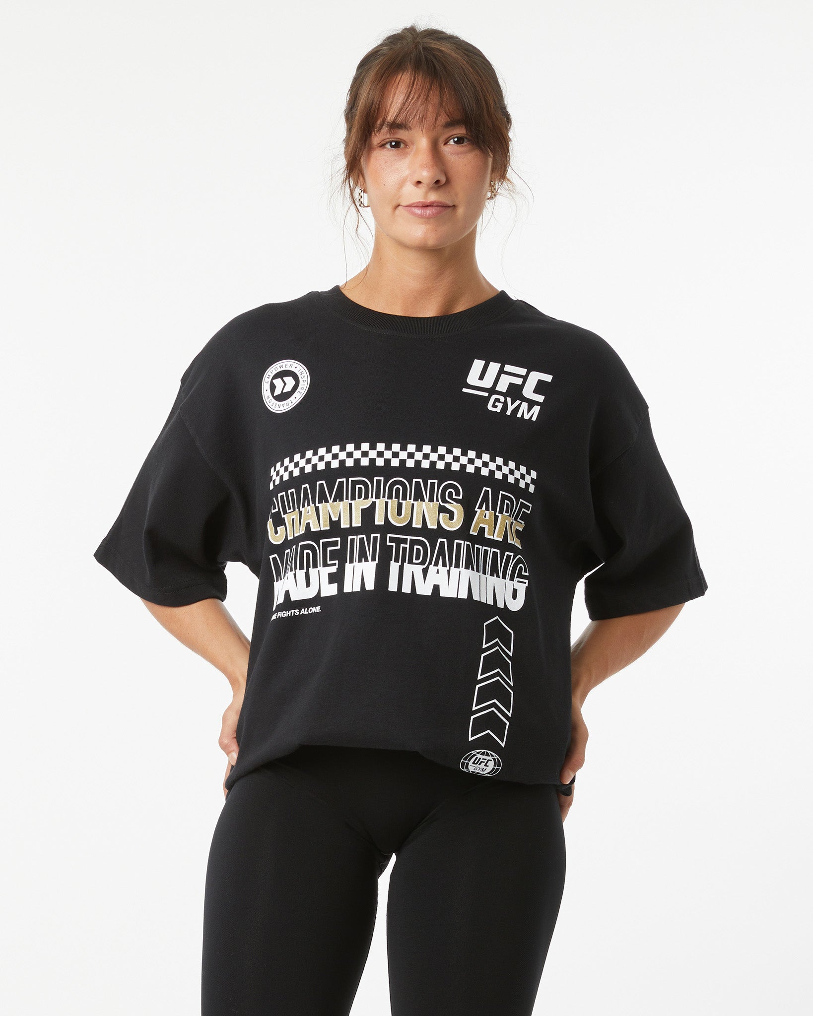 Person wearing a black UFC Gym t-shirt with text on a white background with her hands on her hips