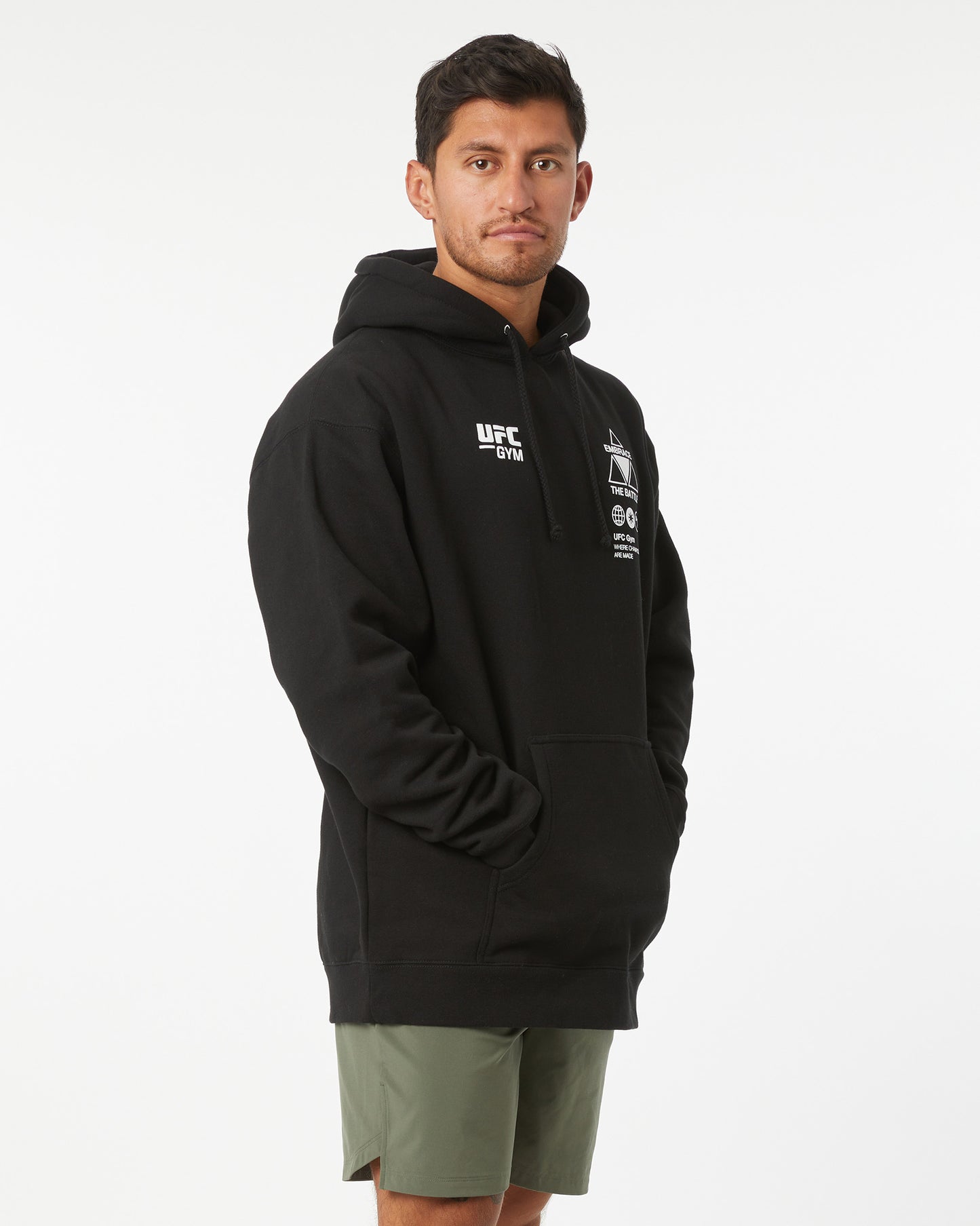 Man wearing a black UFC hoodie with a white logo on a white background facing right looking forward