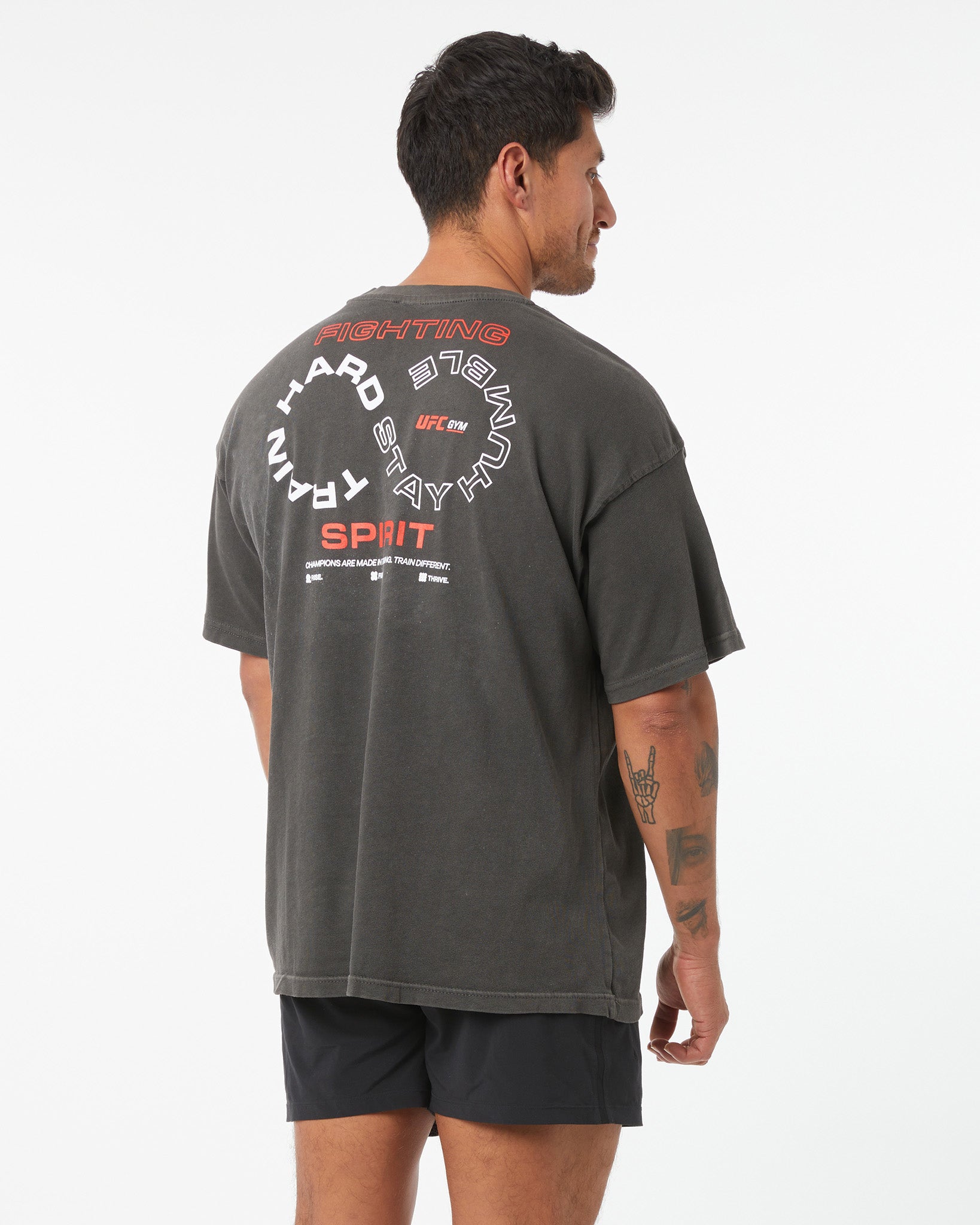 Person wearing a dark gray t-shirt with text on the back, standing against a white background