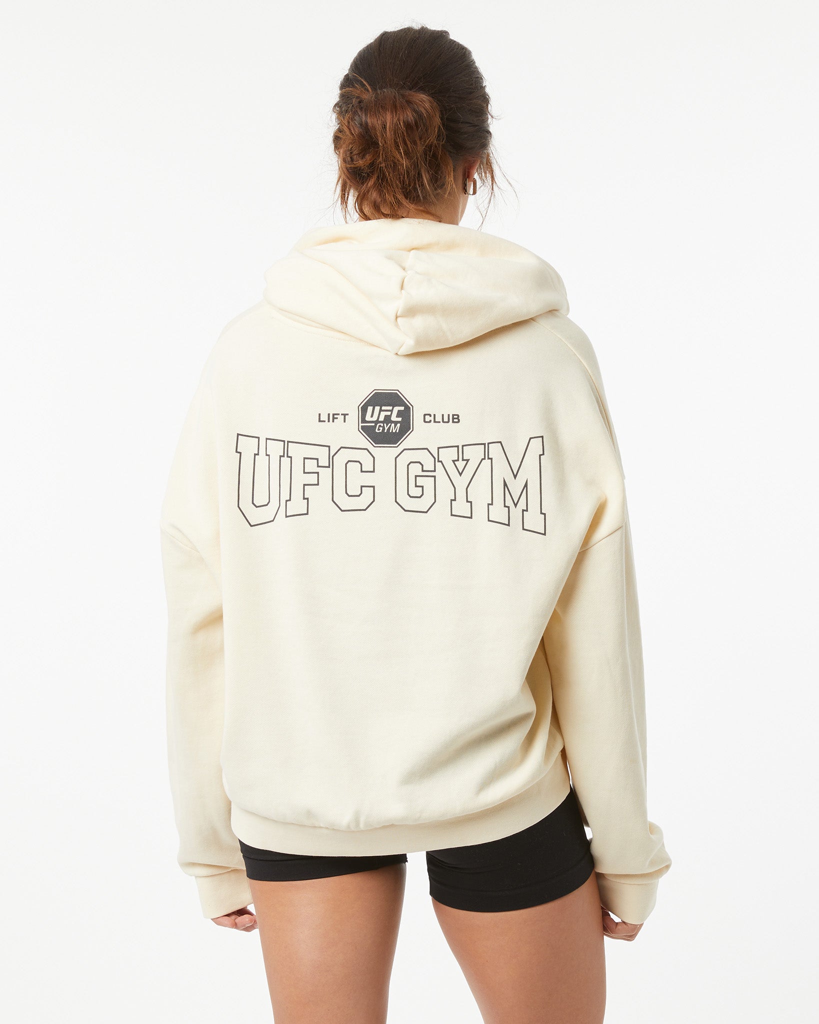 Woman wearing a bone white hoodie with 'UFC Gym' text on the back, on a white background