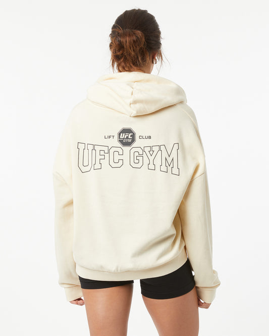Woman wearing a bone white hoodie with 'UFC Gym' text on the back, on a white background