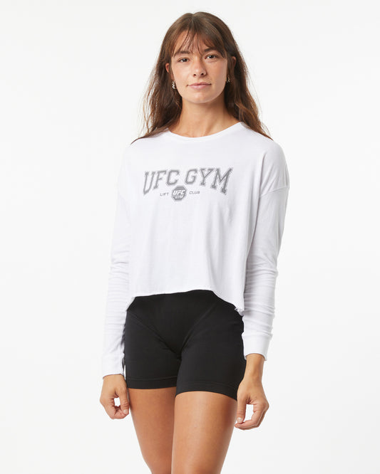 Woman wearing a white UFC Gym long-sleeve shirt and black shorts on a white background