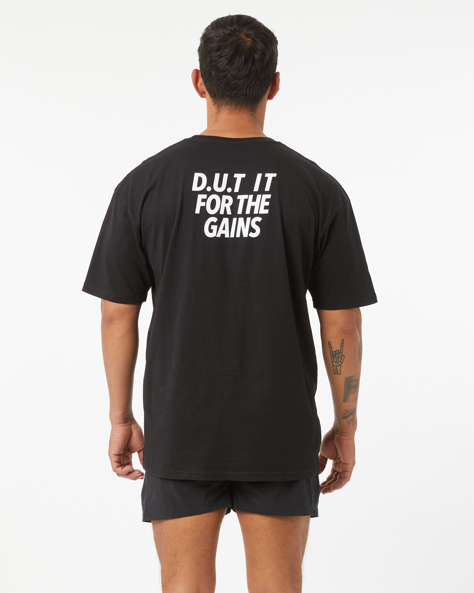 Person wearing a black t-shirt with 'D.U.T. IT FOR THE GAINS' text on the back.