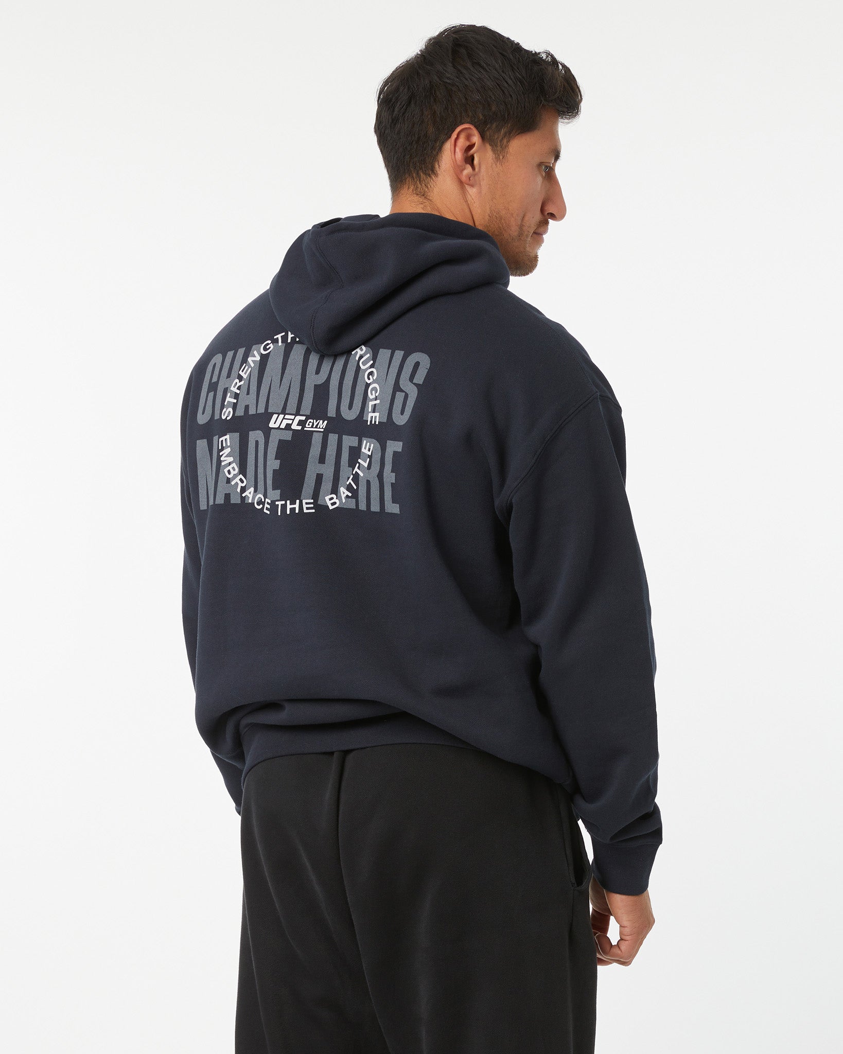 Man wearing a black hoodie with train different, strength in struggle text with a UFC GYM logo on the back, standing against a white background